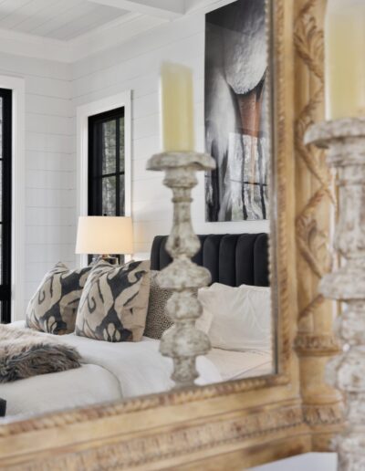 A cozy bedroom interior reflected in a framed mirror with elegant candlesticks on the foreground.
